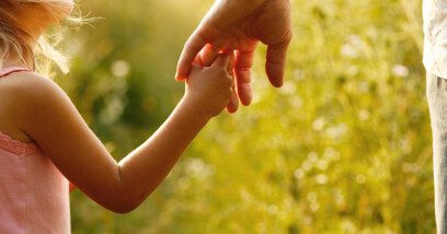 A parent holds the hand of a small child