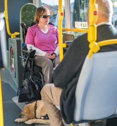 Genevieve McLachlan sits in her power wheelchair with her guide dog on an accessible bus
