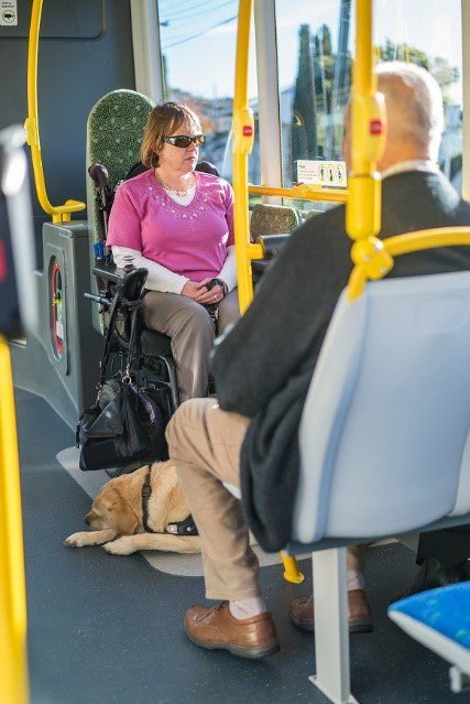 Genevieve McLachlan sits in her power wheelchair with her guide dog on an accessible bus