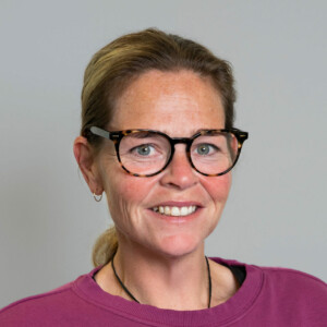 Aimee Lloyd wears glasses and a fuchsiashirt, with her hair pulled back.
