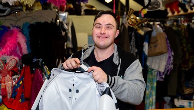 A man with down syndrome holds up a shirt. He seems excited.